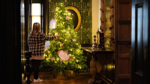 Woman looking at a decoratively twinkling Christmas tree in a historic room